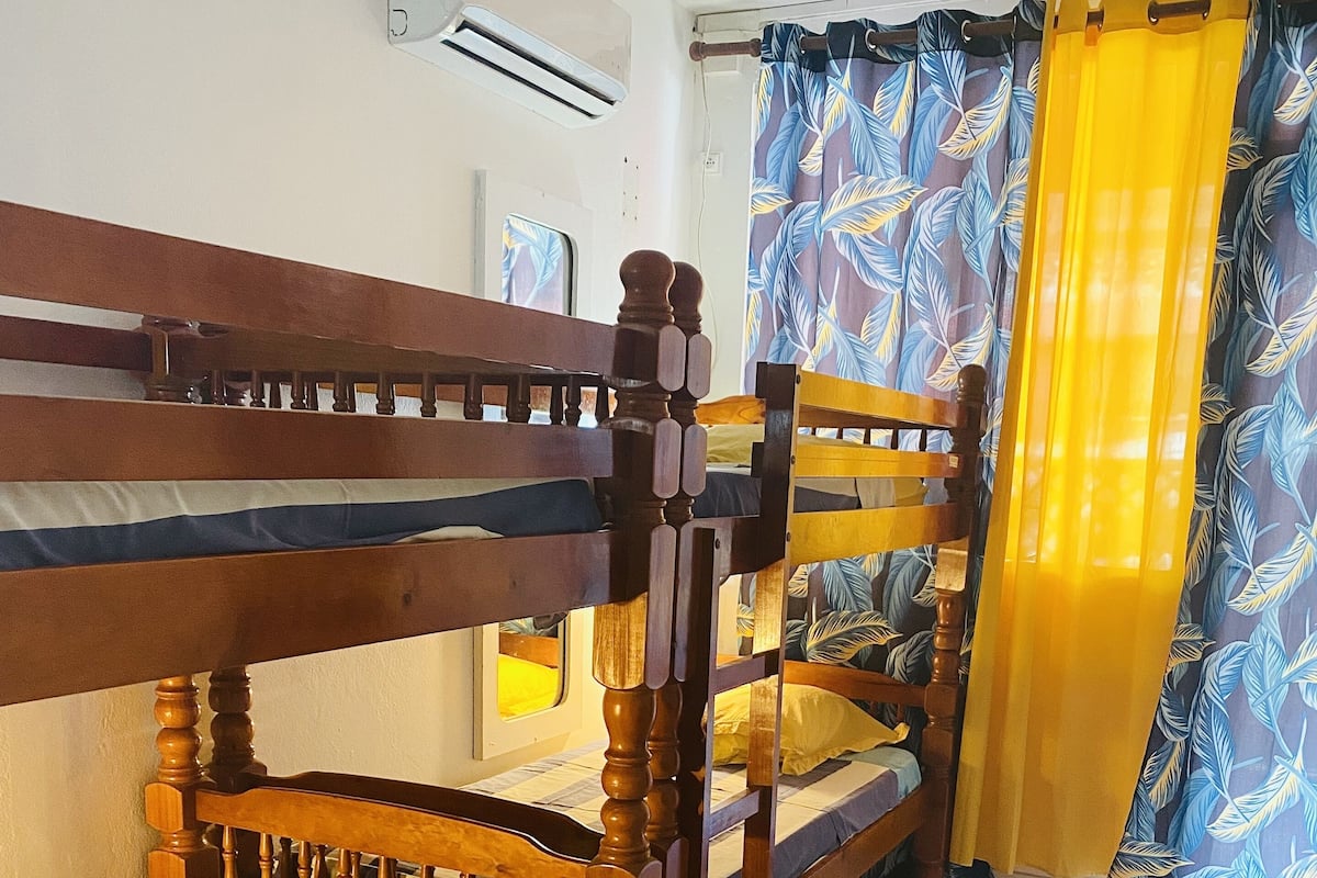 Quarto com beliches, piso de azulejos e janela com cortinas.