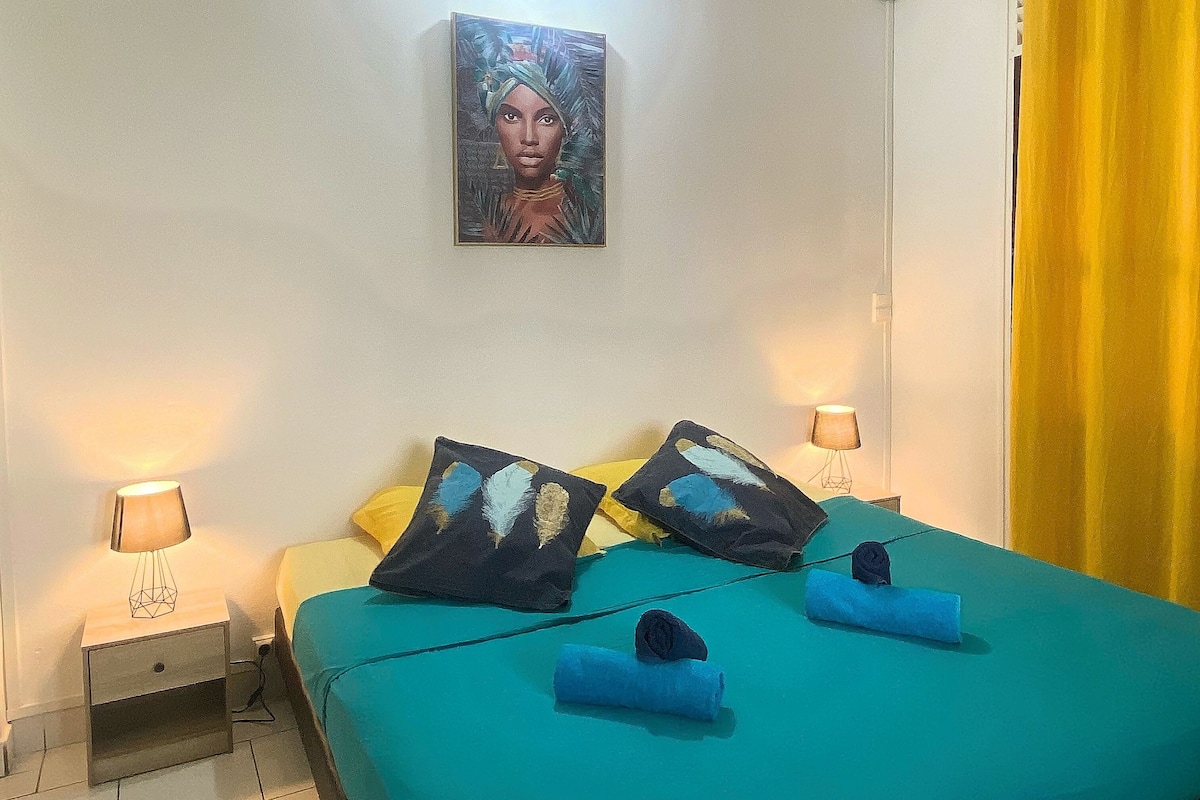Uma cama bem arrumada com roupa de cama azul-turquesa, dois travesseiros com desenhos de penas e uma pintura sobre a cama.