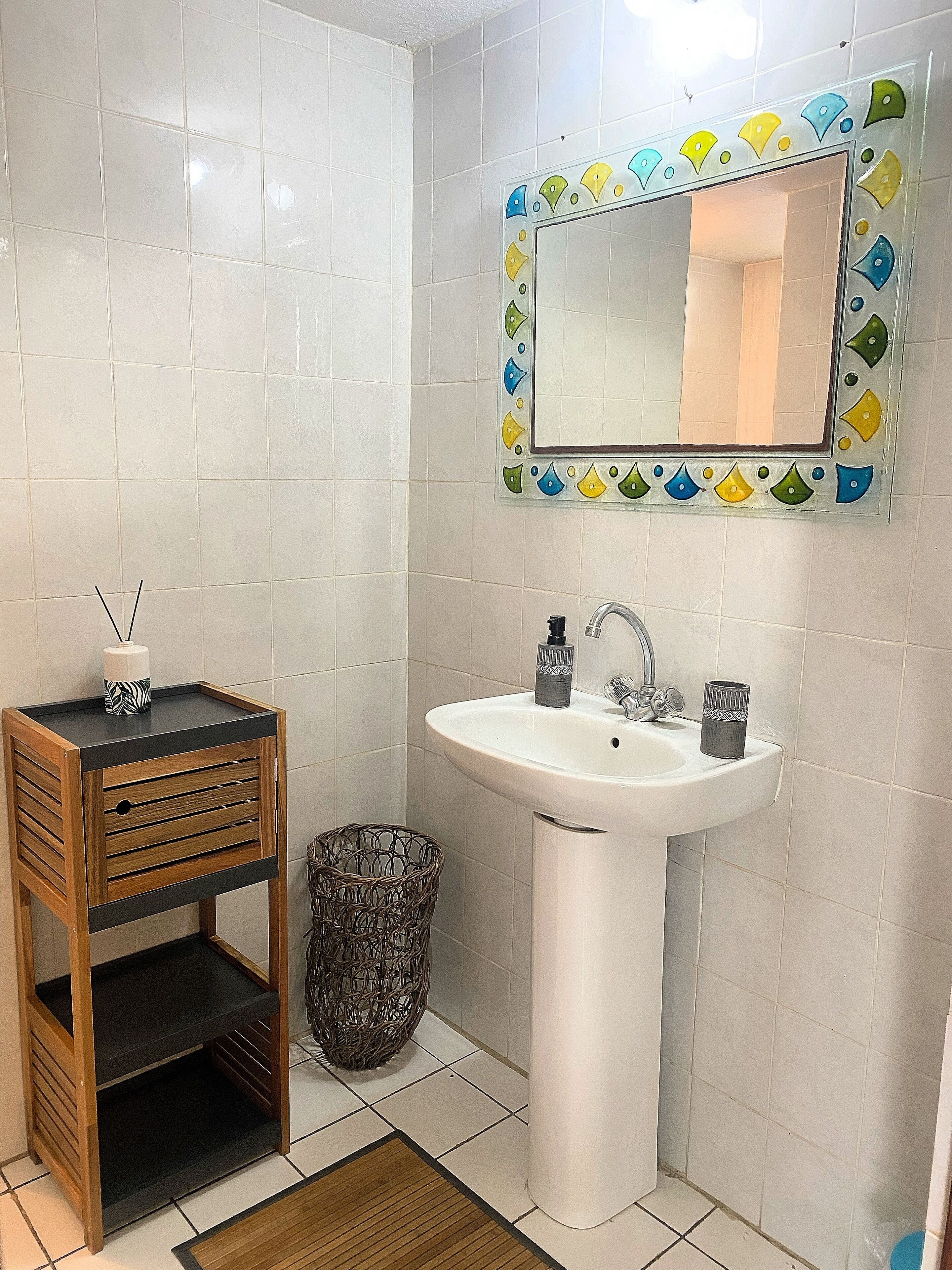 Un bagno con un mobile vanitario in legno, un lavandino bianco e uno specchio con cornice colorata.
