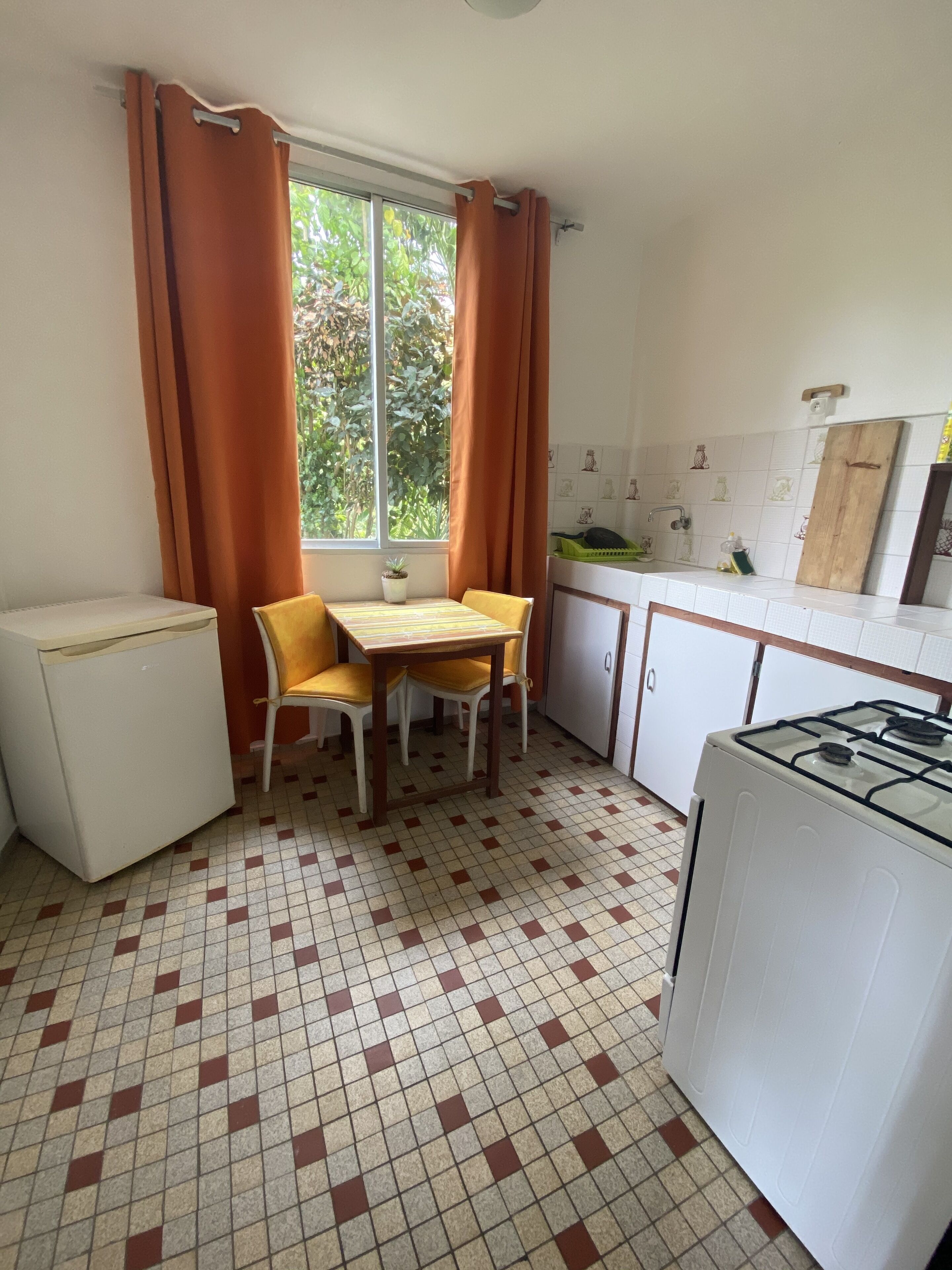 Una cocina compacta con una mesa de comedor, sillas, un refrigerador, una estufa y una ventana con cortinas.