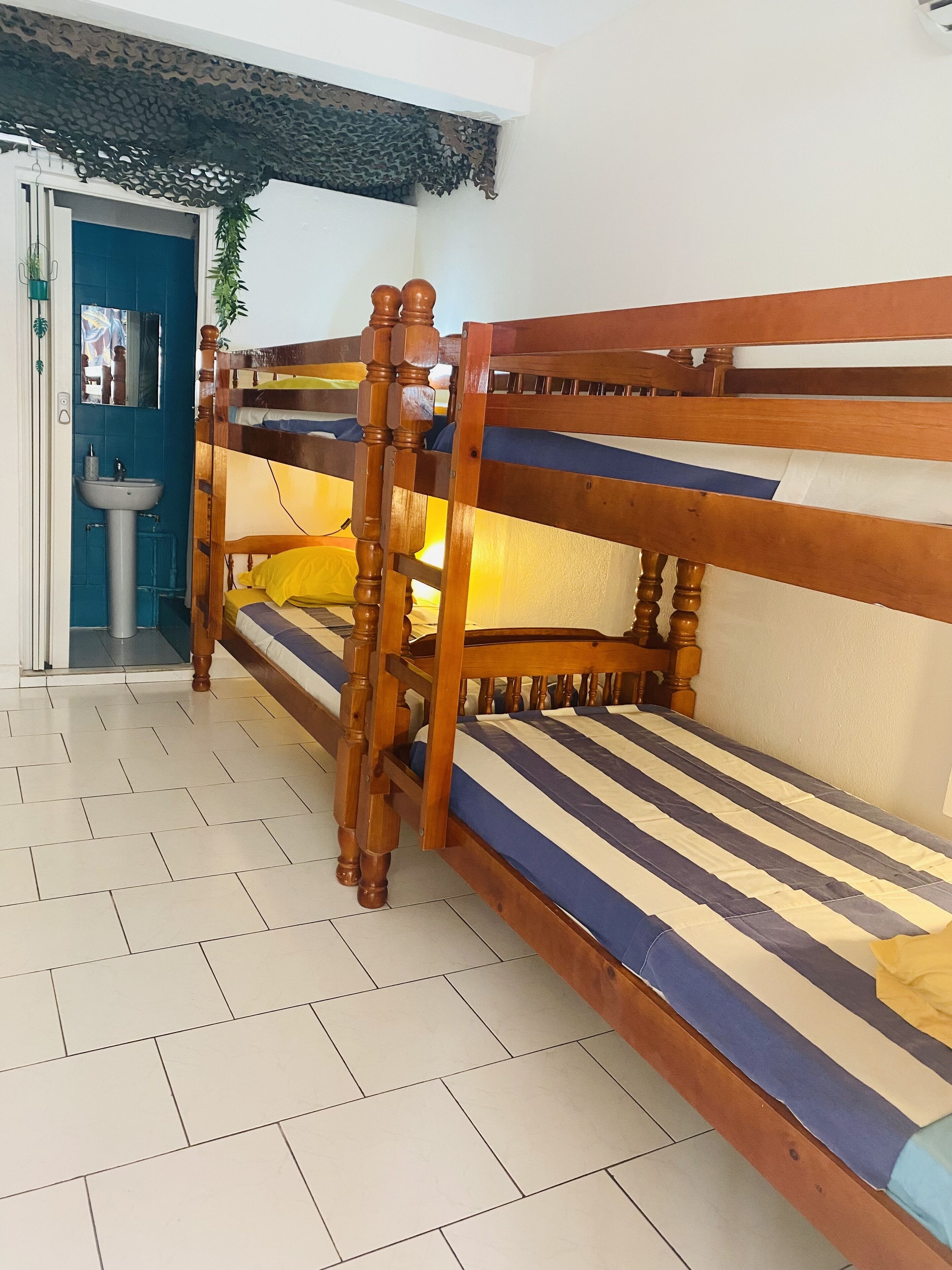 Una cama individual con estructuras de madera y ropa de cama a rayas, un lavabo y una pared con azulejos azules.