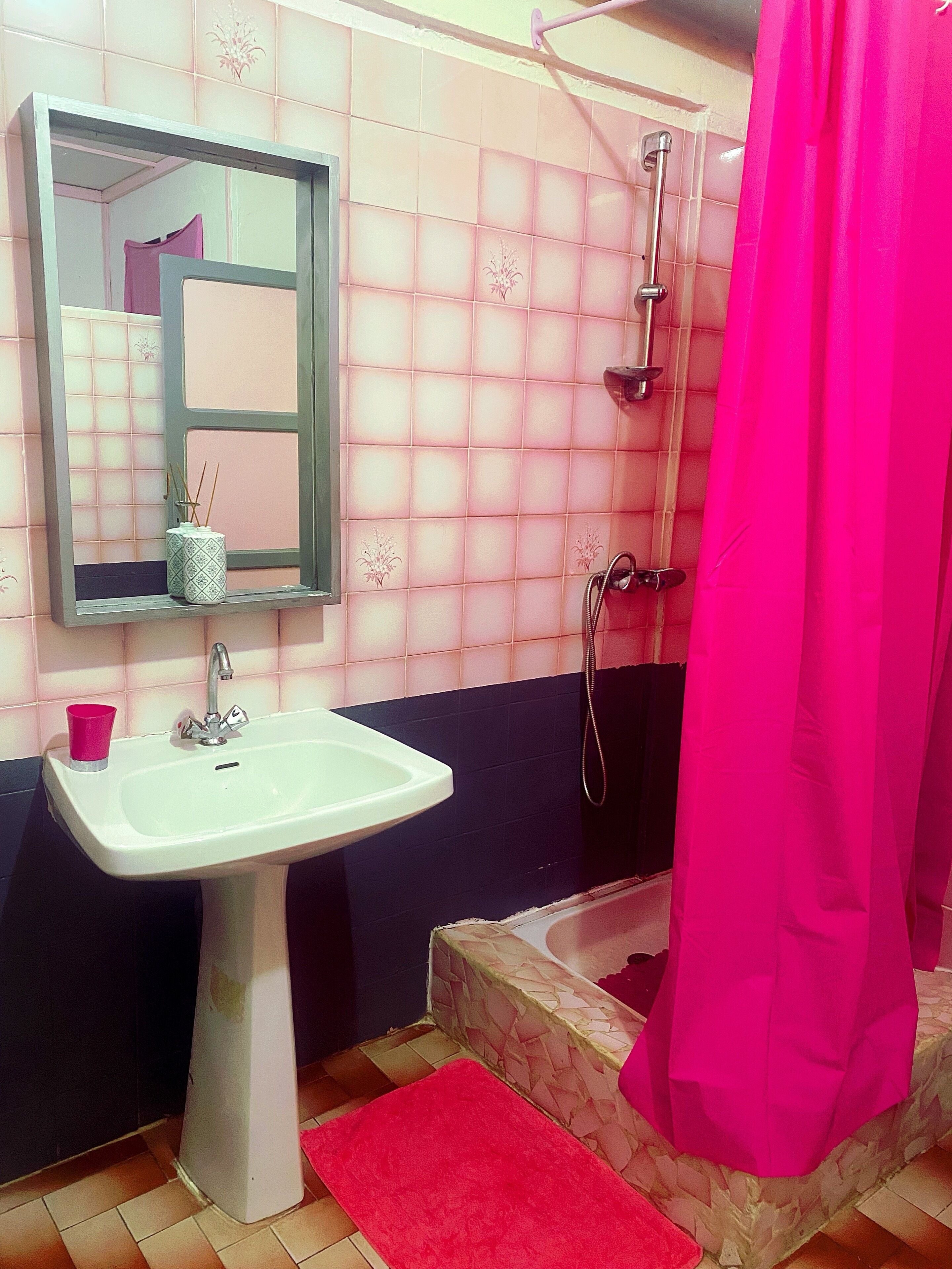A bathroom with a white sink, a mirror, a pink shower curtain, and a red rug.