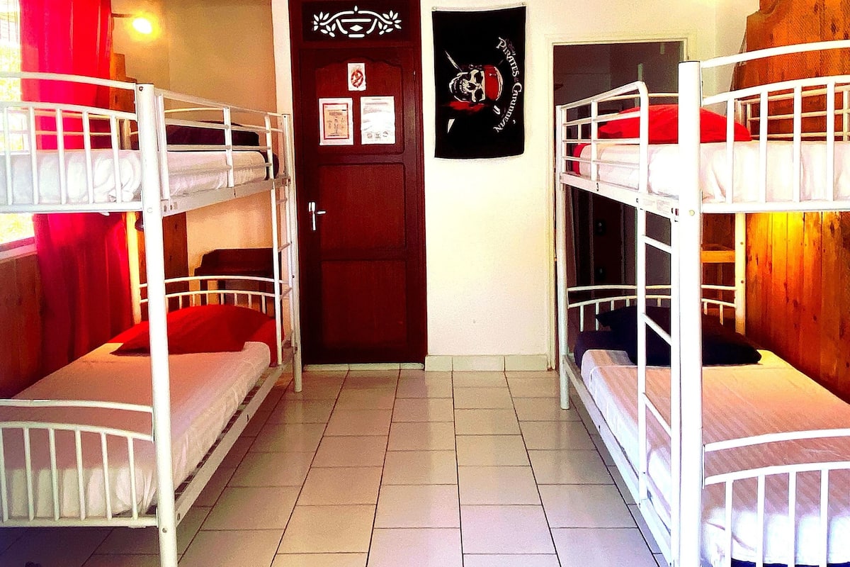 Um dormitório com beliches, uma porta de madeira e um luminário fixado na parede.