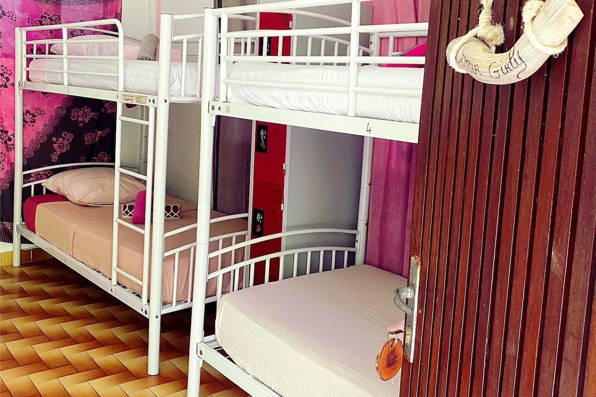 Quarto com beliche, piso de madeira, uma bolsa pendurada e uma porta vermelha.