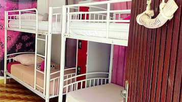 Une chambre avec un lit superposé, un plancher en bois, un sac suspendu et une porte rouge.