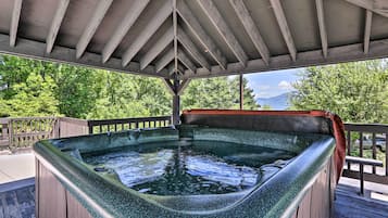 Un bain à remous sous une pergola en bois, avec vue sur les arbres et les montagnes.