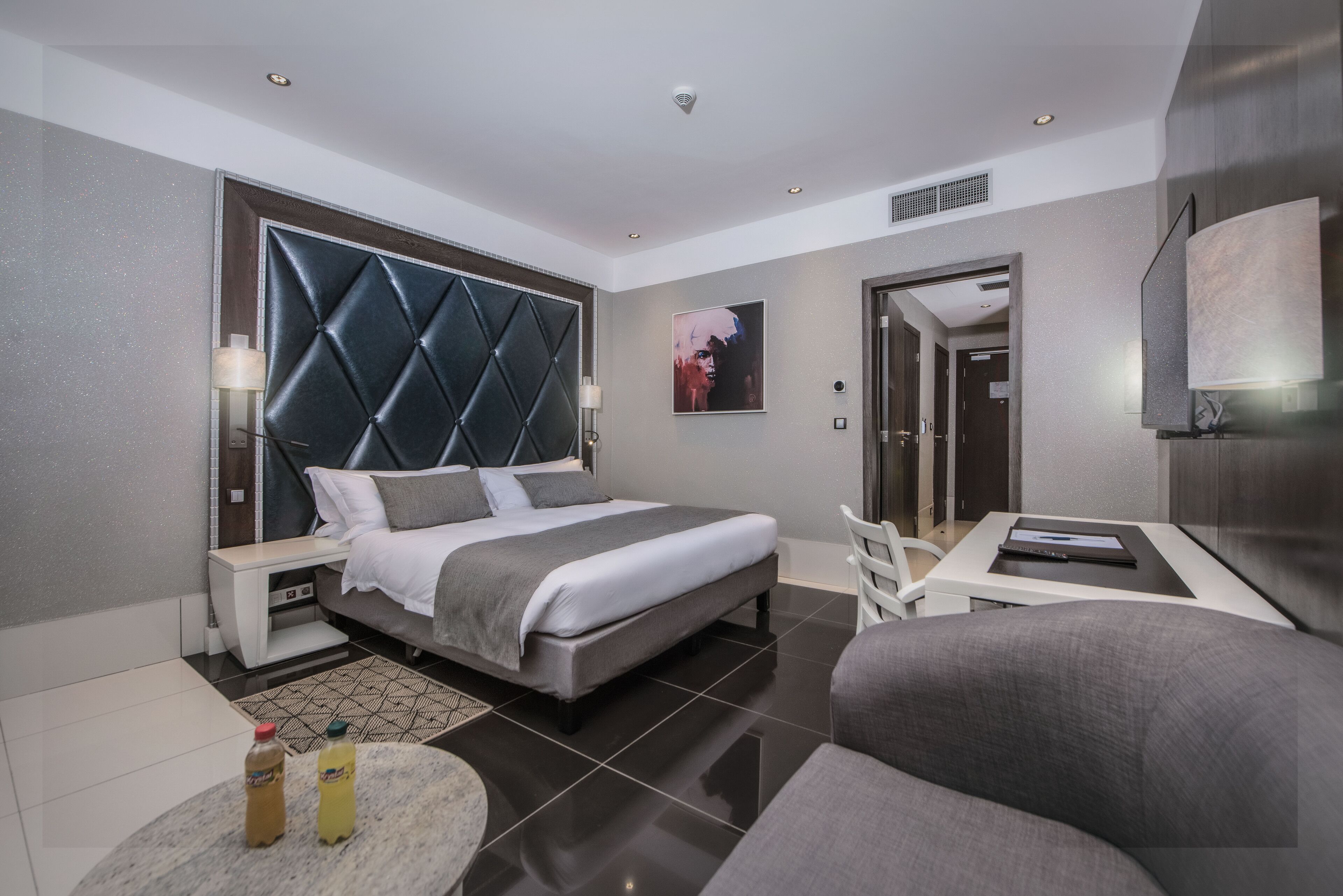 A modern hotel room with a large bed, a desk, a chair, and a flat-screen TV.