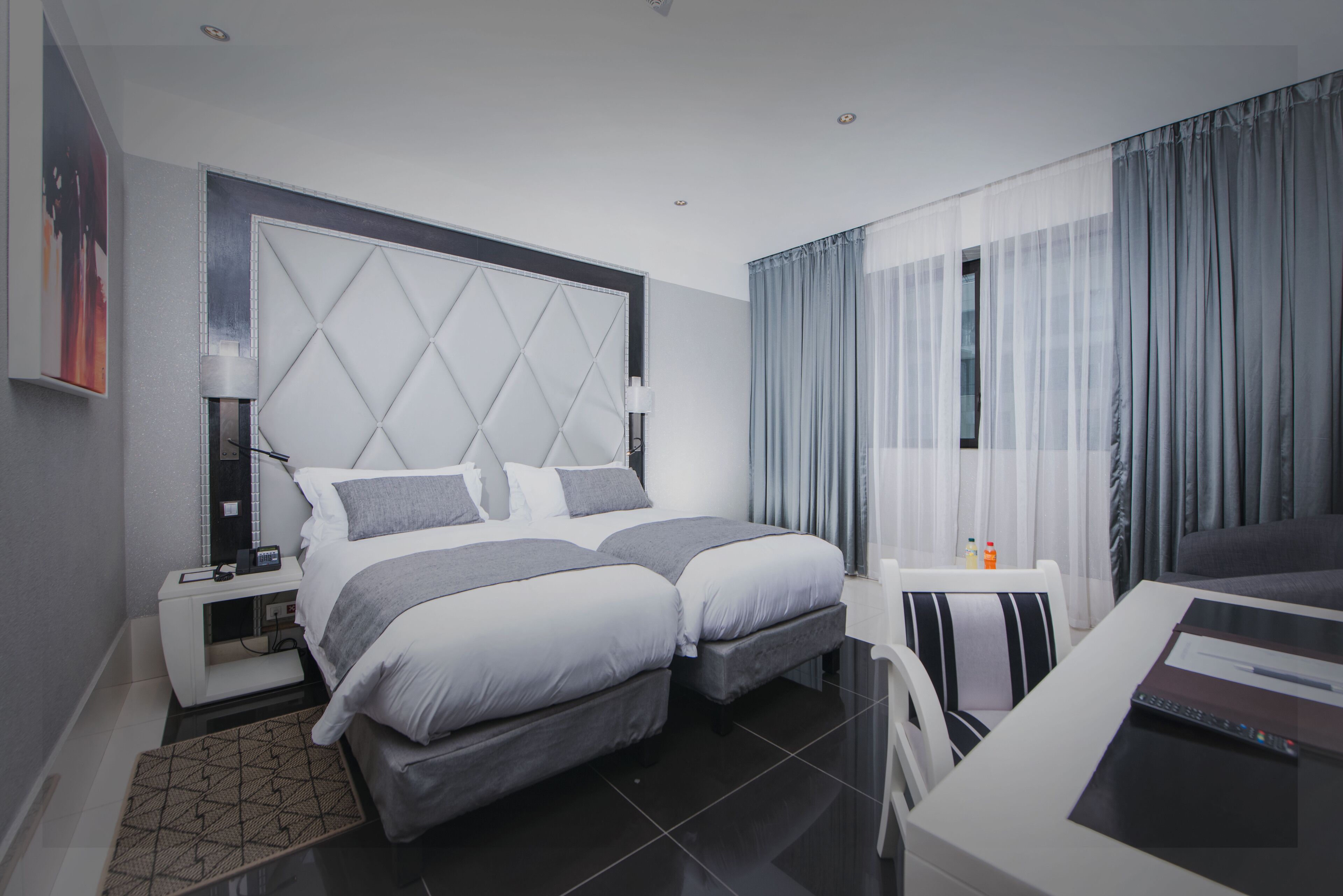 A modern hotel room with a large bed, bedside tables, a desk, and a window with curtains.