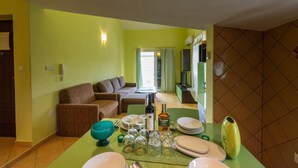 A dining area with a table set for four, a sofa, and a kitchen area in the background. - Apartments Karen (Marina)