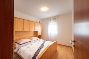 A bedroom with a wooden bed frame, a headboard, and a window with curtains. - Apartments Karen (Marina)