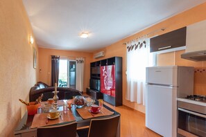 A compact kitchen with a refrigerator, oven, and a dining area with a table set for two. - Apartments Karen (Marina)