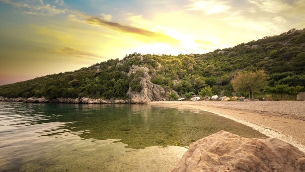 A clear view of a beach with a rocky shoreline and a calm body of water. - Apartments Karen (Marina)