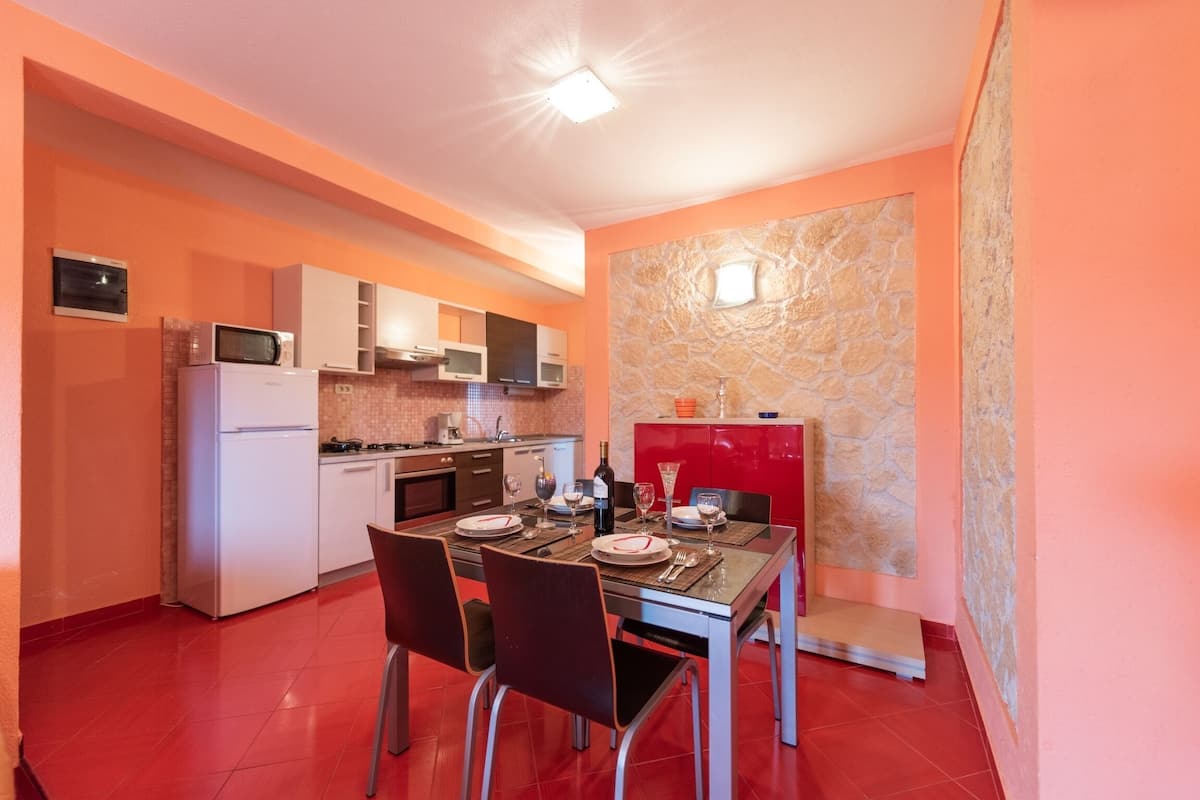 A compact kitchen with a dining area, equipped with a refrigerator, microwave, oven, and a red cabinet.