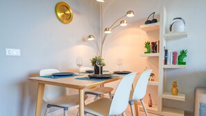 Un coin repas avec une table dressée pour deux personnes, un vase agrémenté de verdure et une bibliothèque contenant des livres et des objets décoratifs.