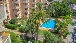 Un immeuble de grande hauteur doté d’une piscine, entouré de palmiers et de verdure.