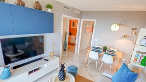 Un salon moderne doté d’un téléviseur à écran plat, d’un coin repas avec une table et des chaises, et d’un espace détente confortable avec un canapé et des coussins.