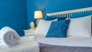 Un lit bien fait, avec des oreillers bleus et blancs, une serviette blanche roulée et une lampe de chevet posée sur une table de nuit.