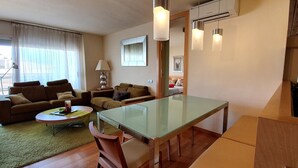 Ein modernes Wohnzimmer mit einem Esstisch mit Glasplatte, Sofas und einem kleinen Couchtisch.