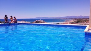 Ein Schwimmbecken mit klarem, blauem Wasser, umgeben von einem Gebäude mit Blick auf das Meer und Berge im Hintergrund.