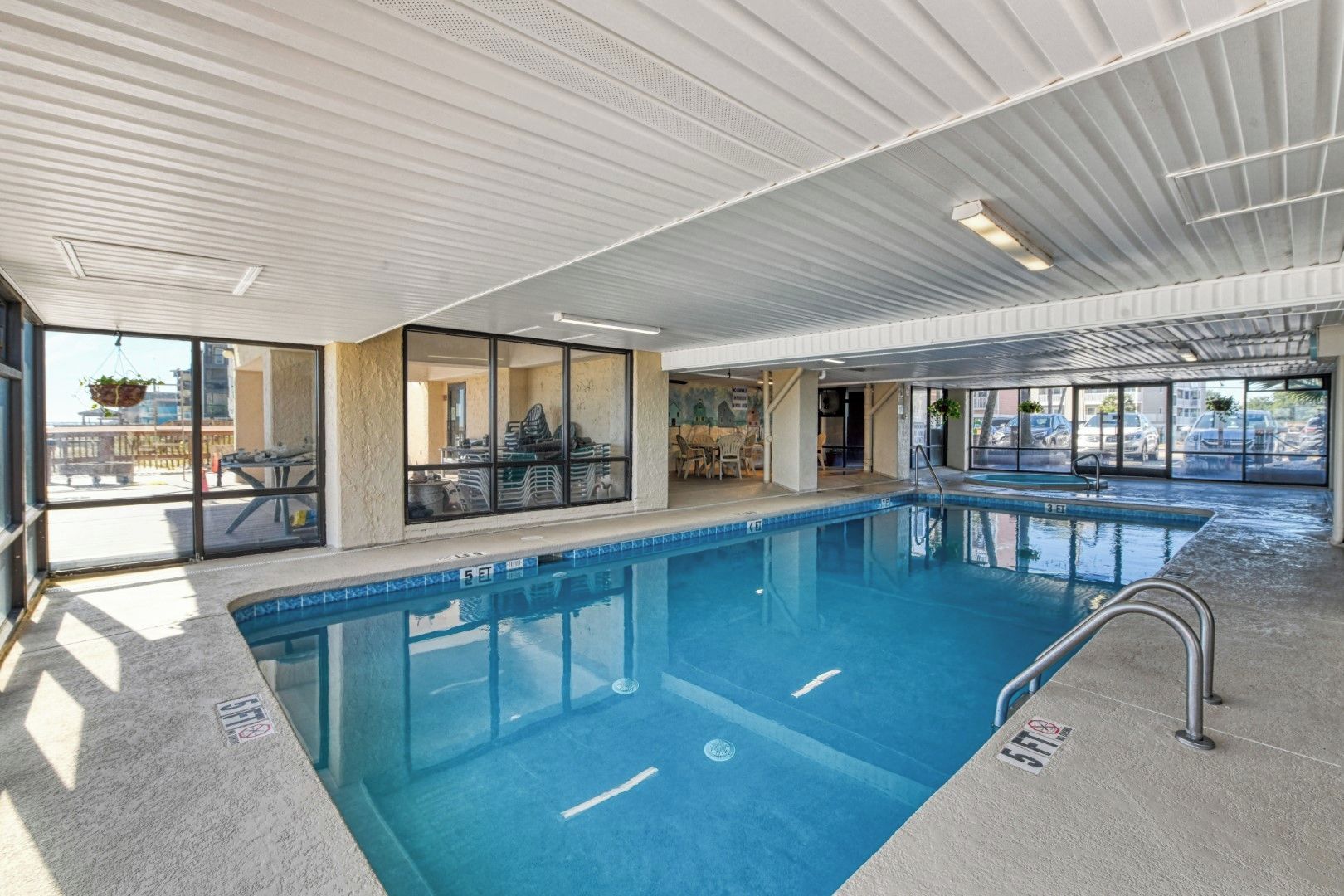 An indoor swimming pool with clear water, a diving board, and a view of the outside.