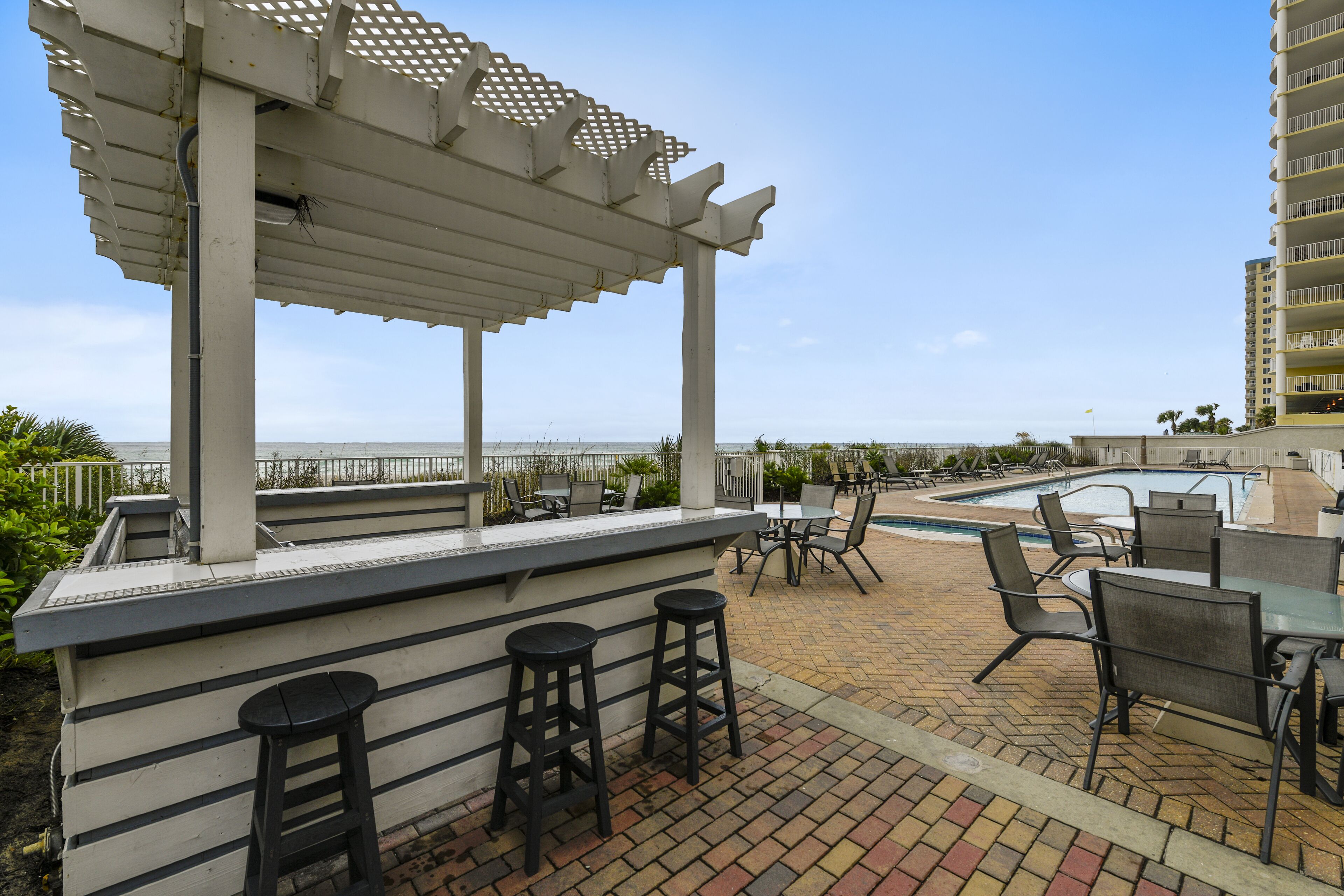 An outdoor bar area with a pool, seating, and a view of the ocean.