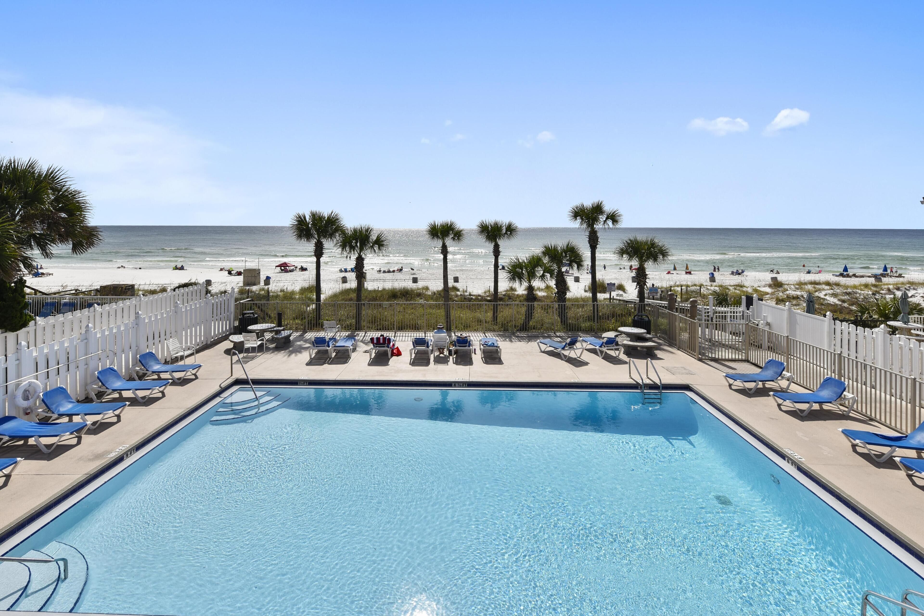 A pool area with blue lounge chairs and a view of the beach.