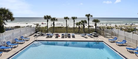 A pool area with blue lounge chairs and a view of the beach.