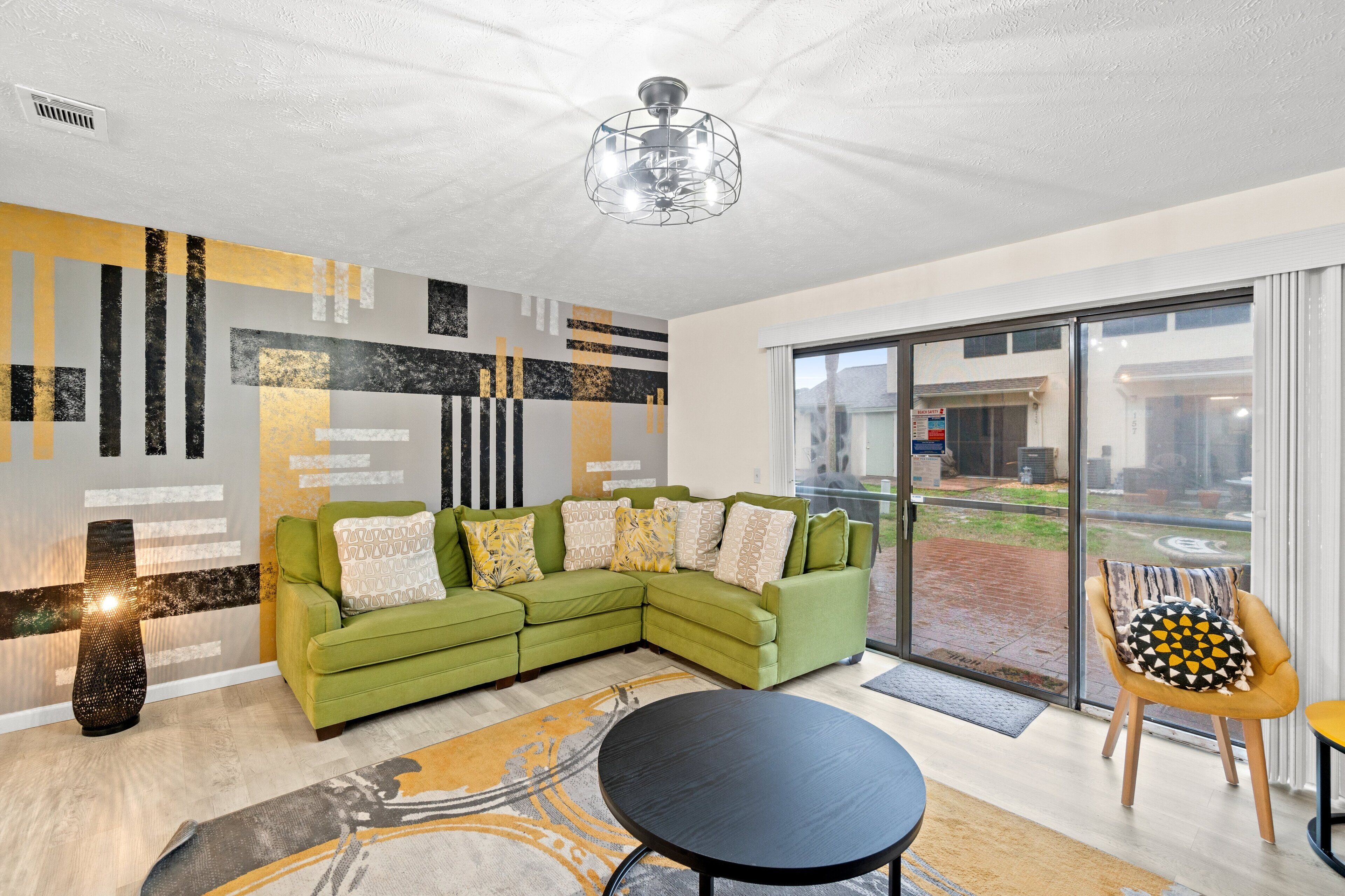 A modern living room with a green sectional sofa, a black coffee table, and a large window offering a view of the outside.
