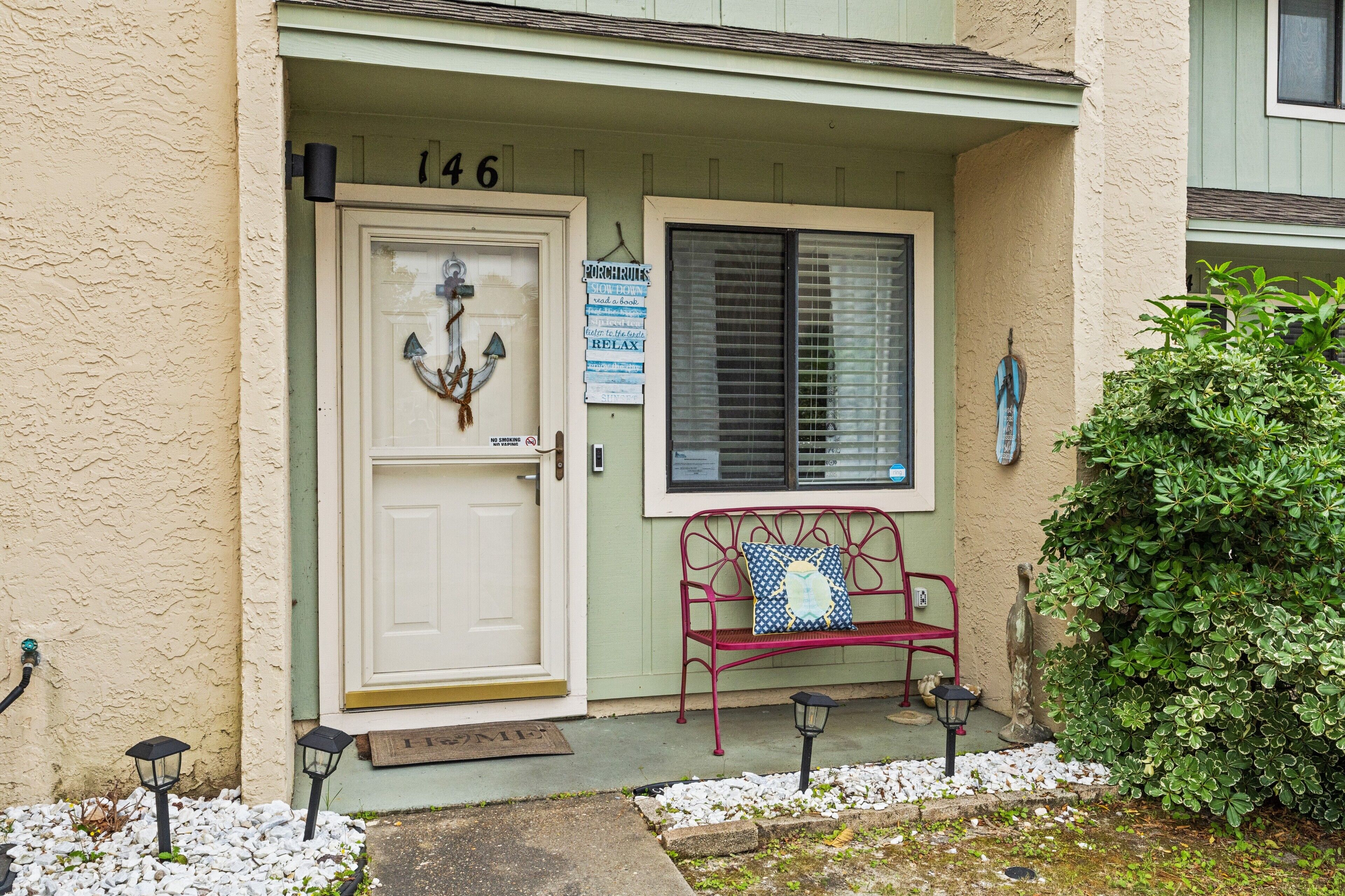 A building entrance with a door labeled "146", a bench, and a small garden area with white pebbles and a green bush.