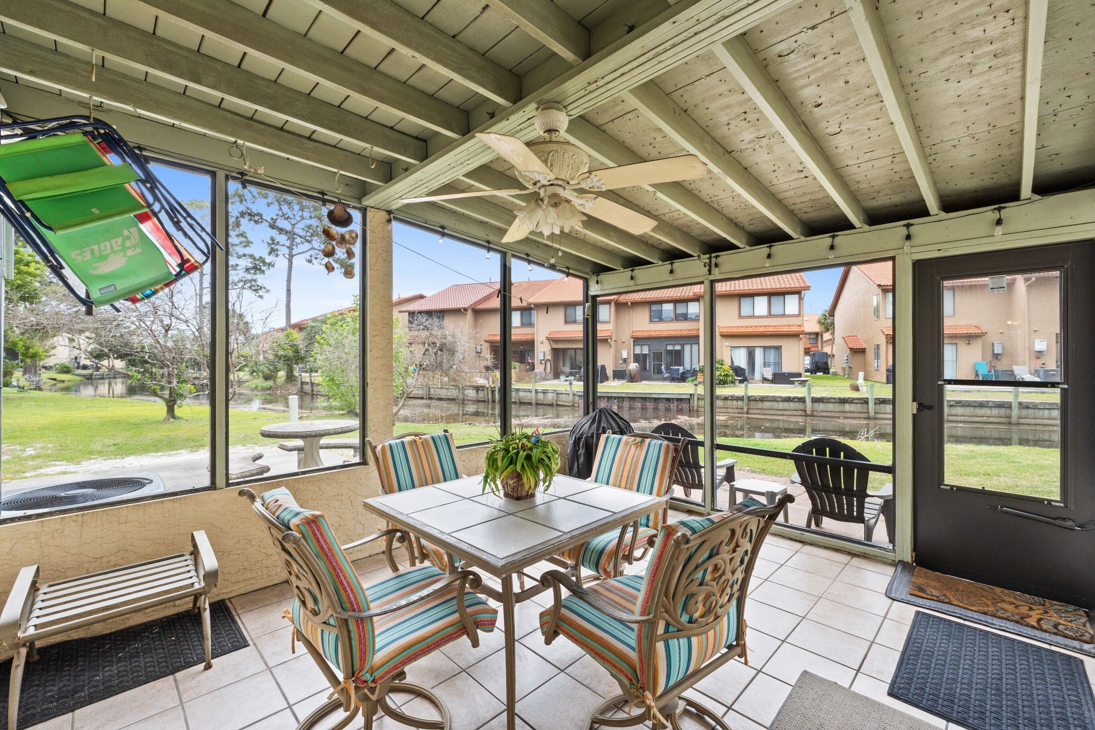 A covered patio area with a table and chairs, a ceiling fan, and a view of the neighborhood.