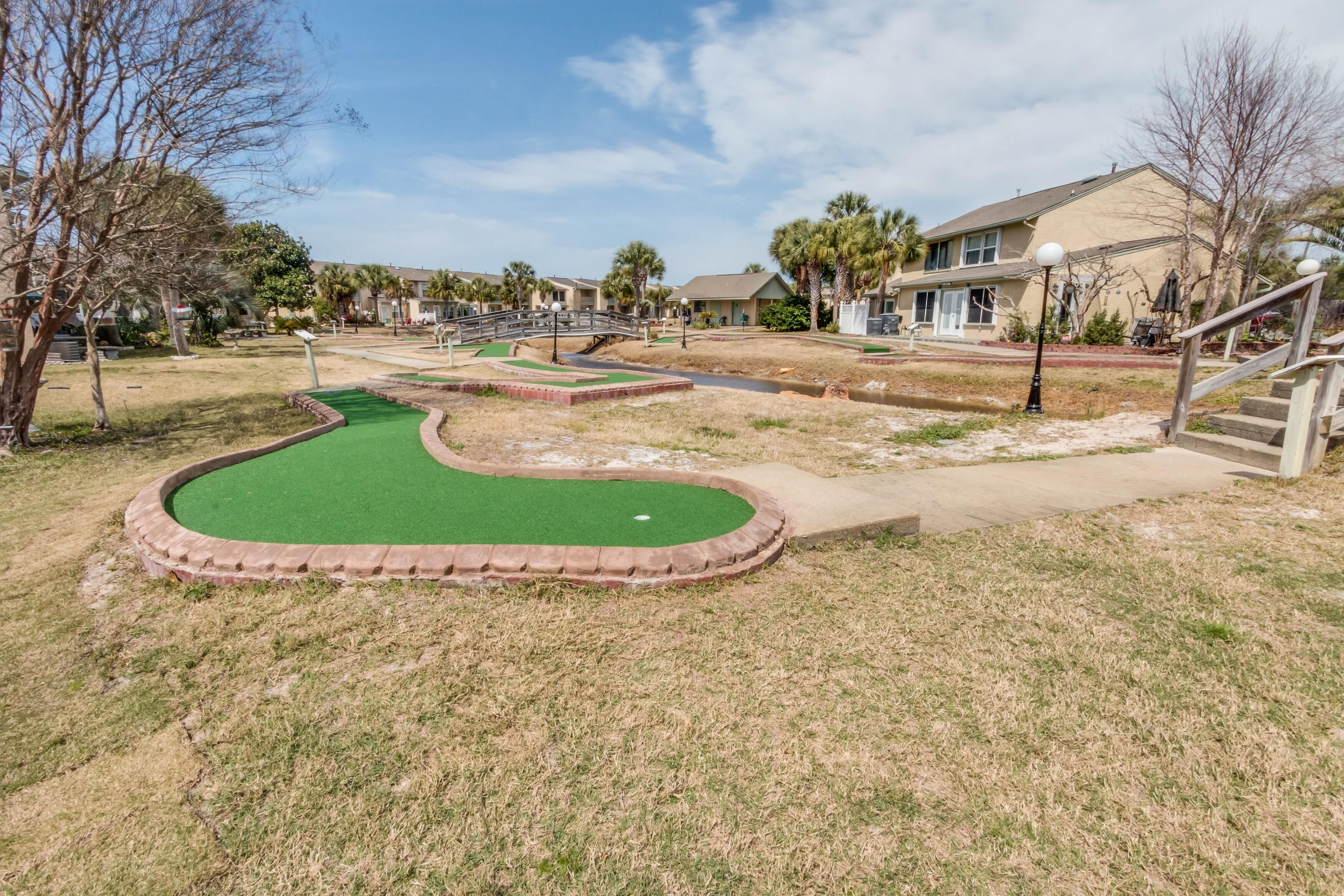 Un parcours de mini-golf avec un pont, entouré de maisons et sous un ciel dégagé.