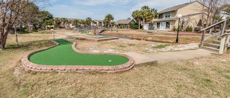 Un parcours de mini-golf avec un pont, entouré de maisons et sous un ciel dégagé.