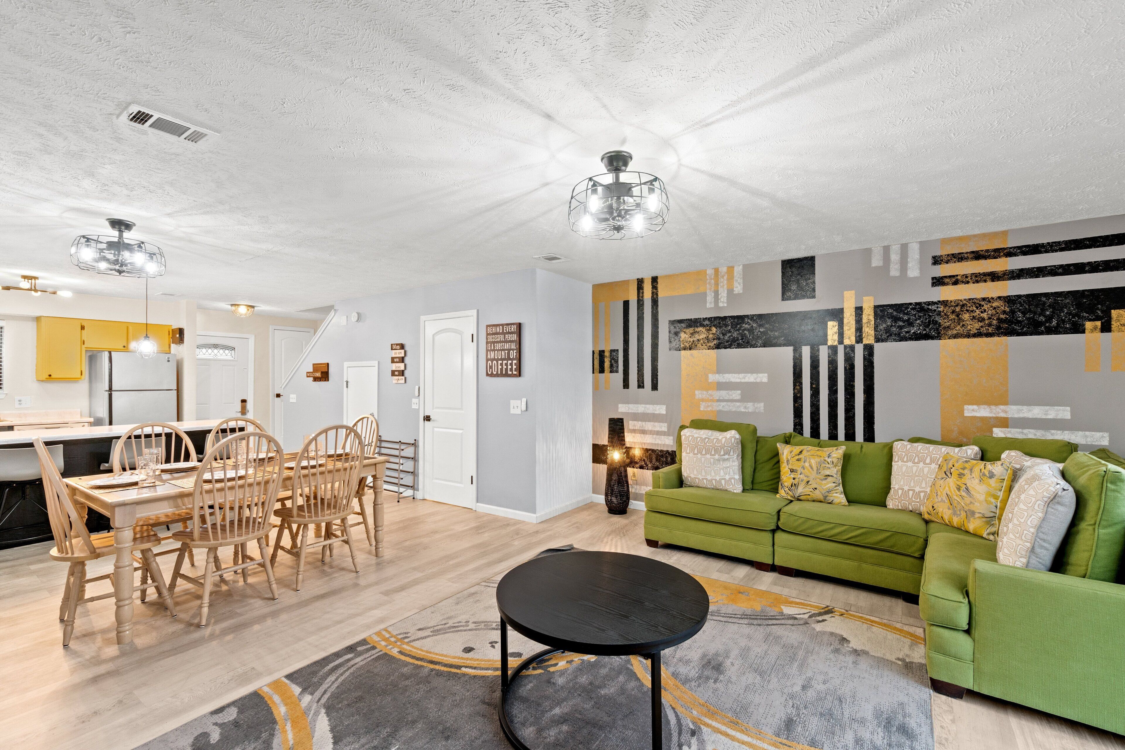 A modern living room with a green sofa, wooden dining table, and chairs. There is a black coffee table in the center.
