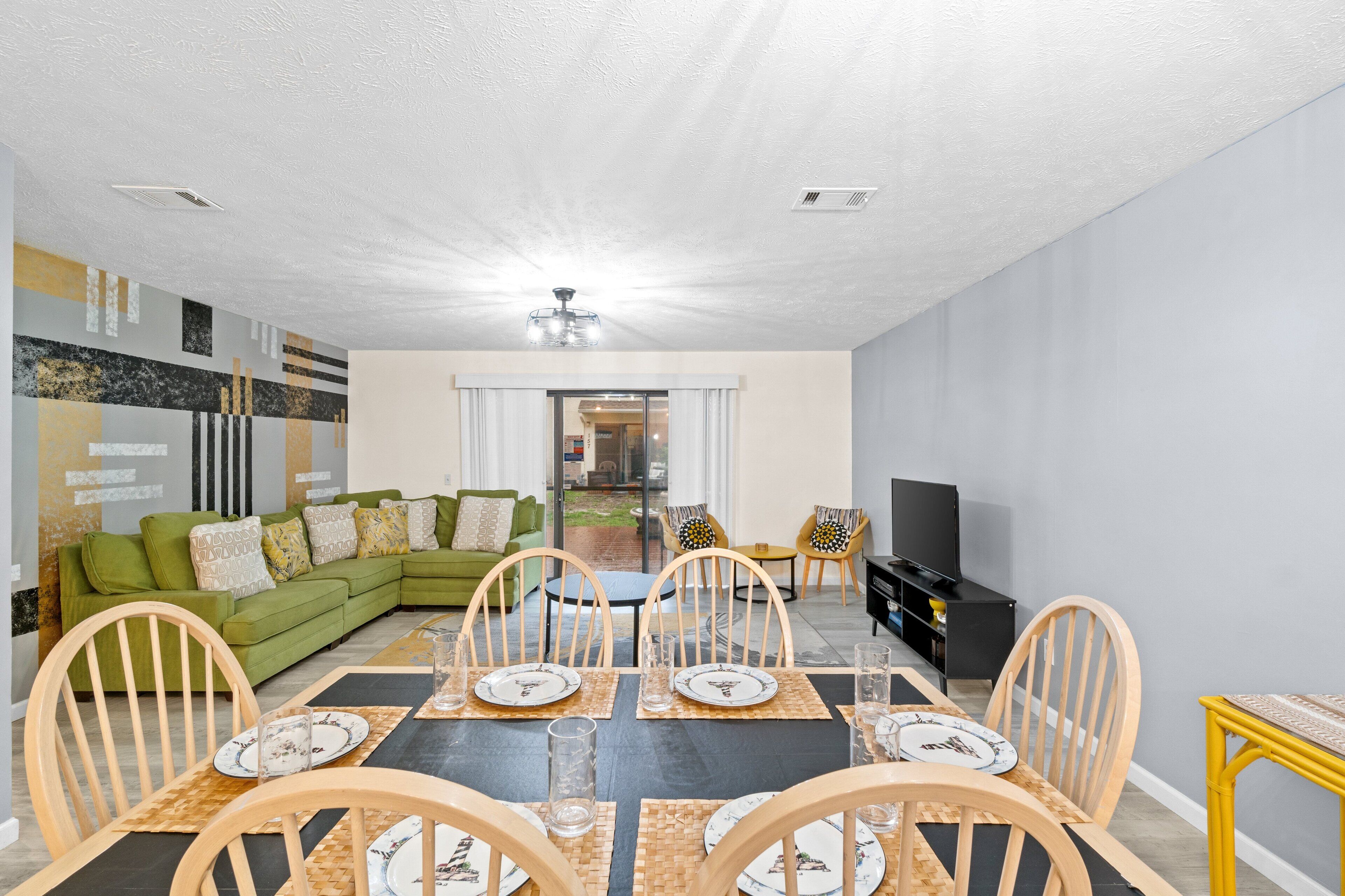 En moderne stue med spiseplads, grøn sofa, træstole og et fjernsyn.