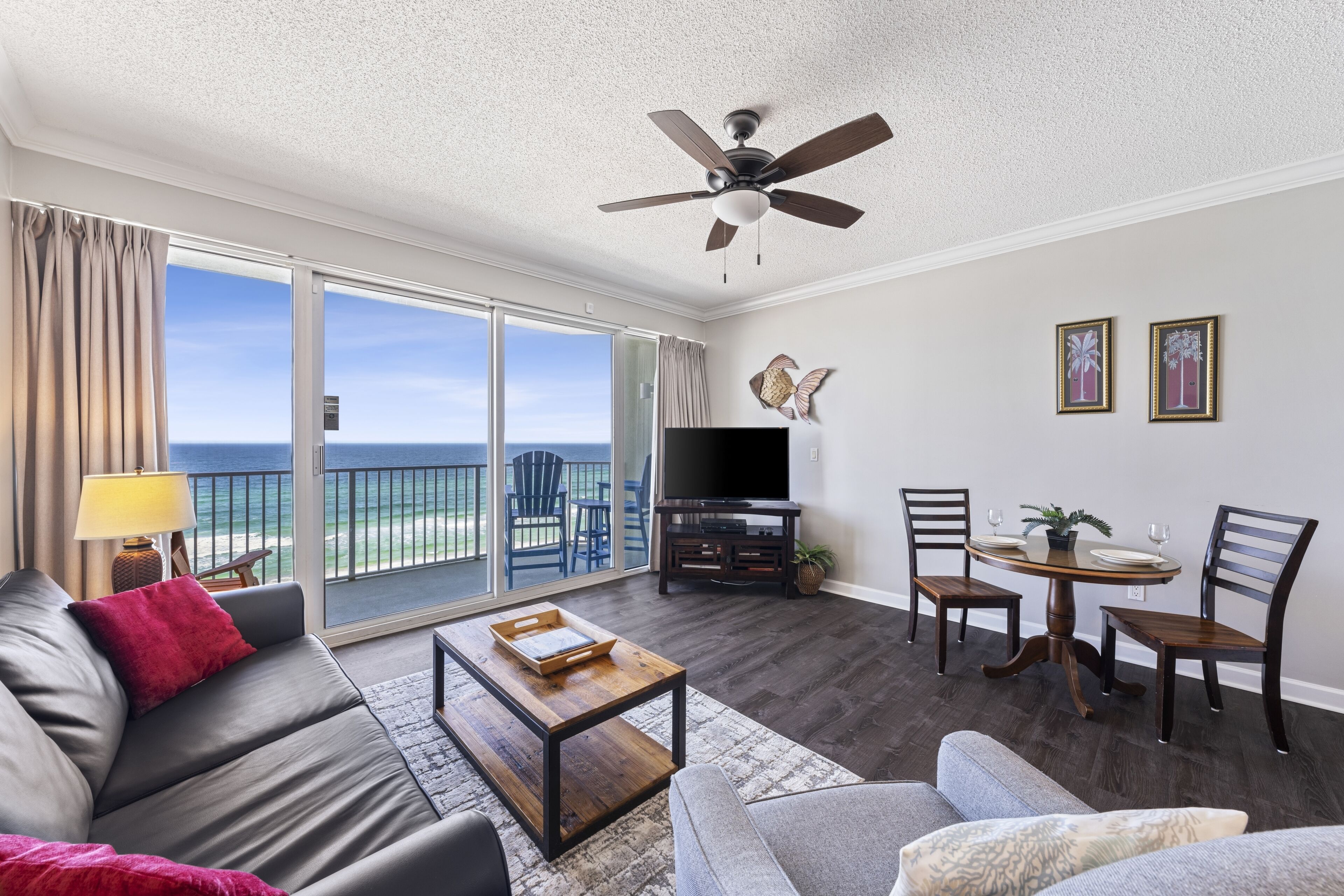 Ein geräumiges Wohnzimmer mit Balkon, Deckenventilator, Flachbildfernseher und Essbereich mit Stühlen und Tisch.