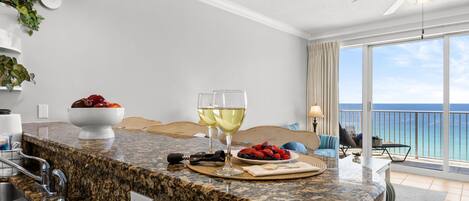 A kitchen with granite countertops, a dining area with a view of the ocean, and a ceiling fan.