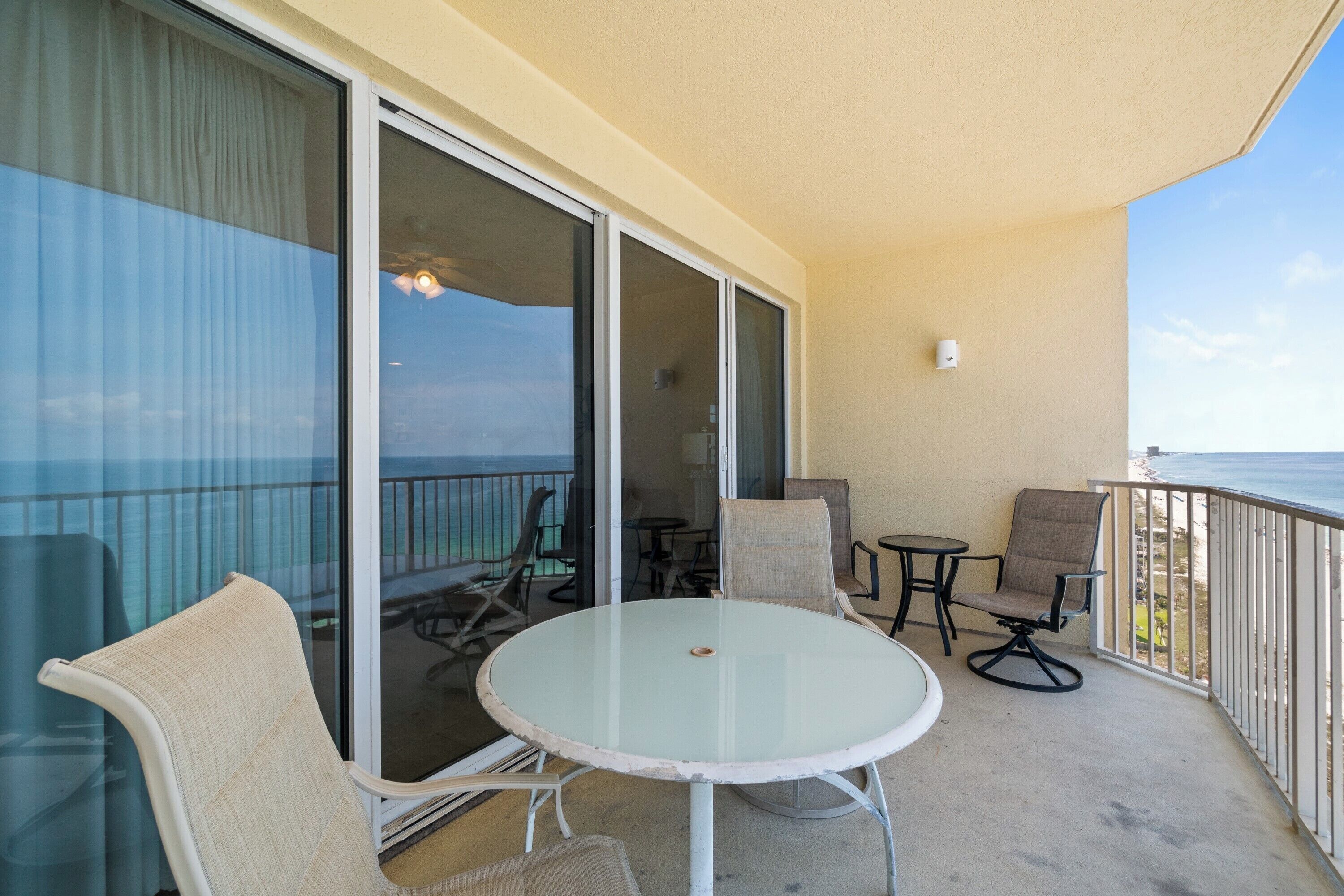 Een balkon met een glazen tafel en stoelen, een klein rond tafeltje, en uitzicht op de oceaan.