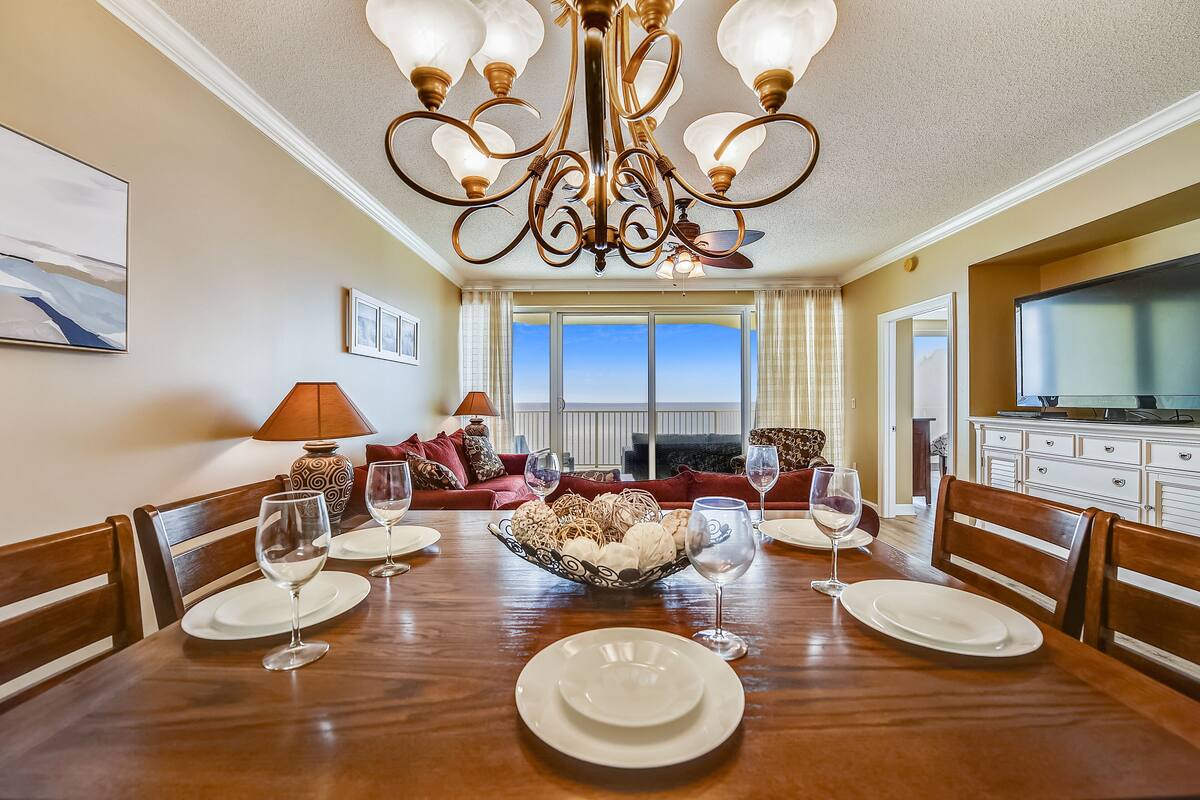 Comedor con mesa de madera dispuesta para cuatro personas, rodeada de sillas, con una araña colgante.