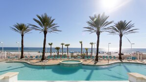 Ein Poolbereich mit Palmen, Liegestühlen und Blick auf den Strand.
