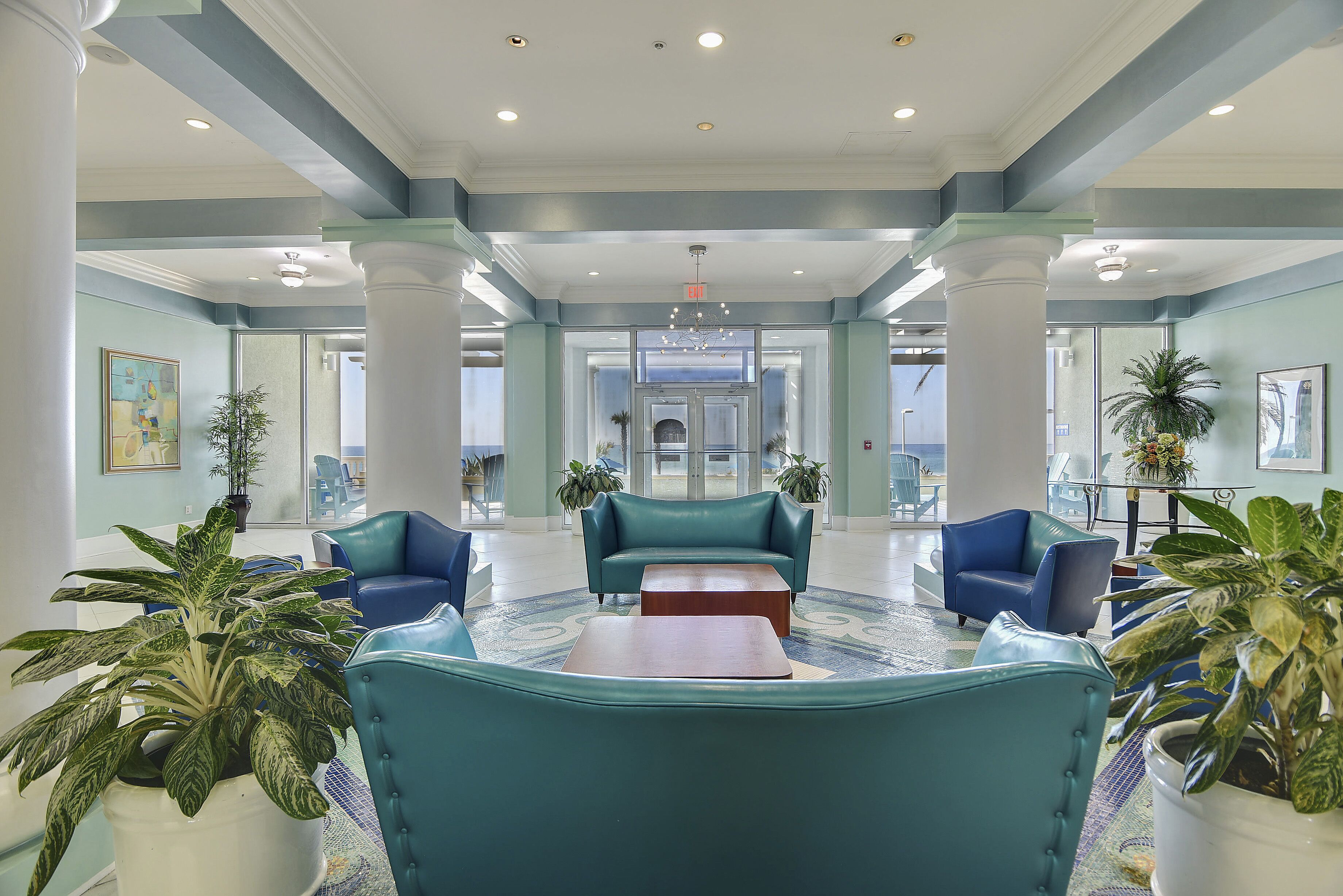 A lobby with teal sofas, a coffee table, and potted plants.