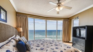 Ein Schlafzimmer mit einem Bett, einer Kommode, einem Deckenventilator und einem großen Fenster mit Blick aufs Meer.