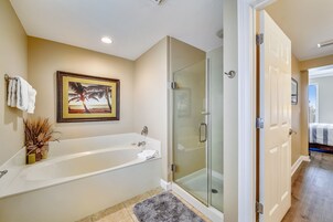 A modern bathroom with a glass-enclosed shower, a large bathtub, and a framed picture on the wall.