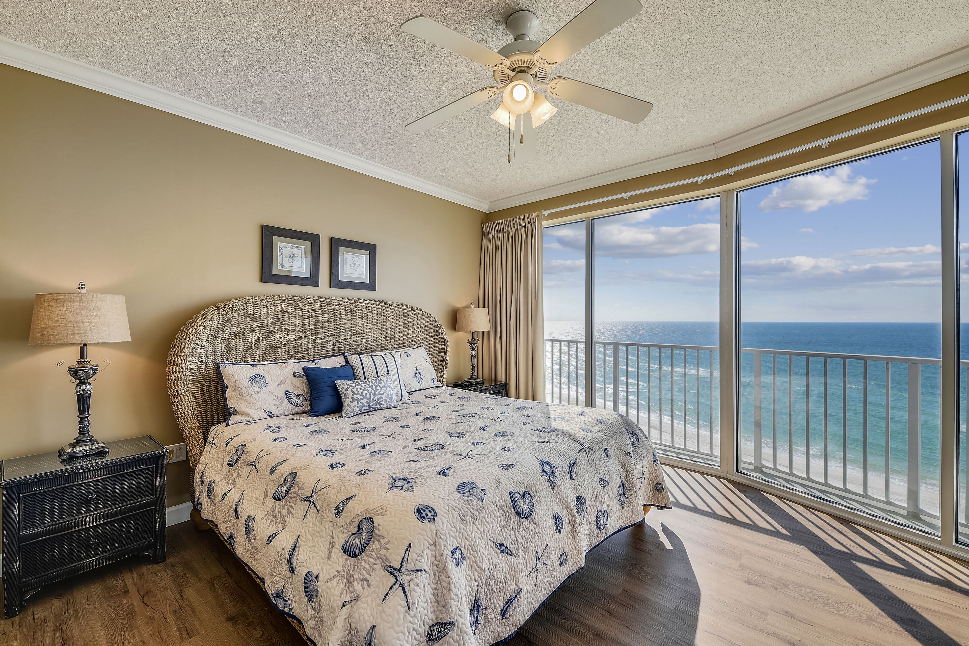 A bedroom with a large bed, a ceiling fan, and a view of the ocean.