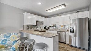 A modern kitchen with white cabinets, a stainless steel refrigerator, and a granite countertop.