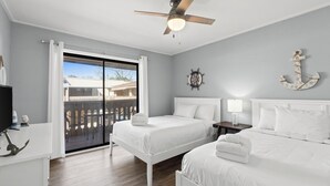 A hotel room with two beds, a ceiling fan, a view through a sliding glass door, and nautical decor.