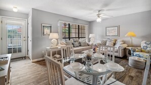 A living room with a dining table set for four, a sofa, a coffee table, and a ceiling fan.