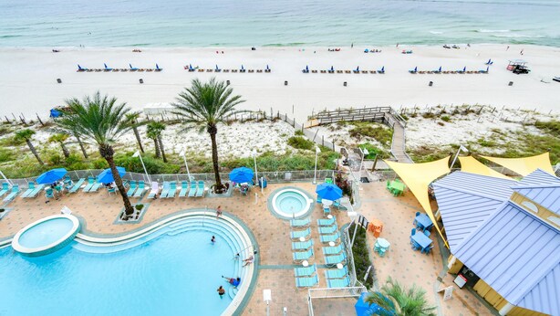 A resort with a swimming pool, beach umbrellas, lounge chairs, and a view of the beach and ocean.