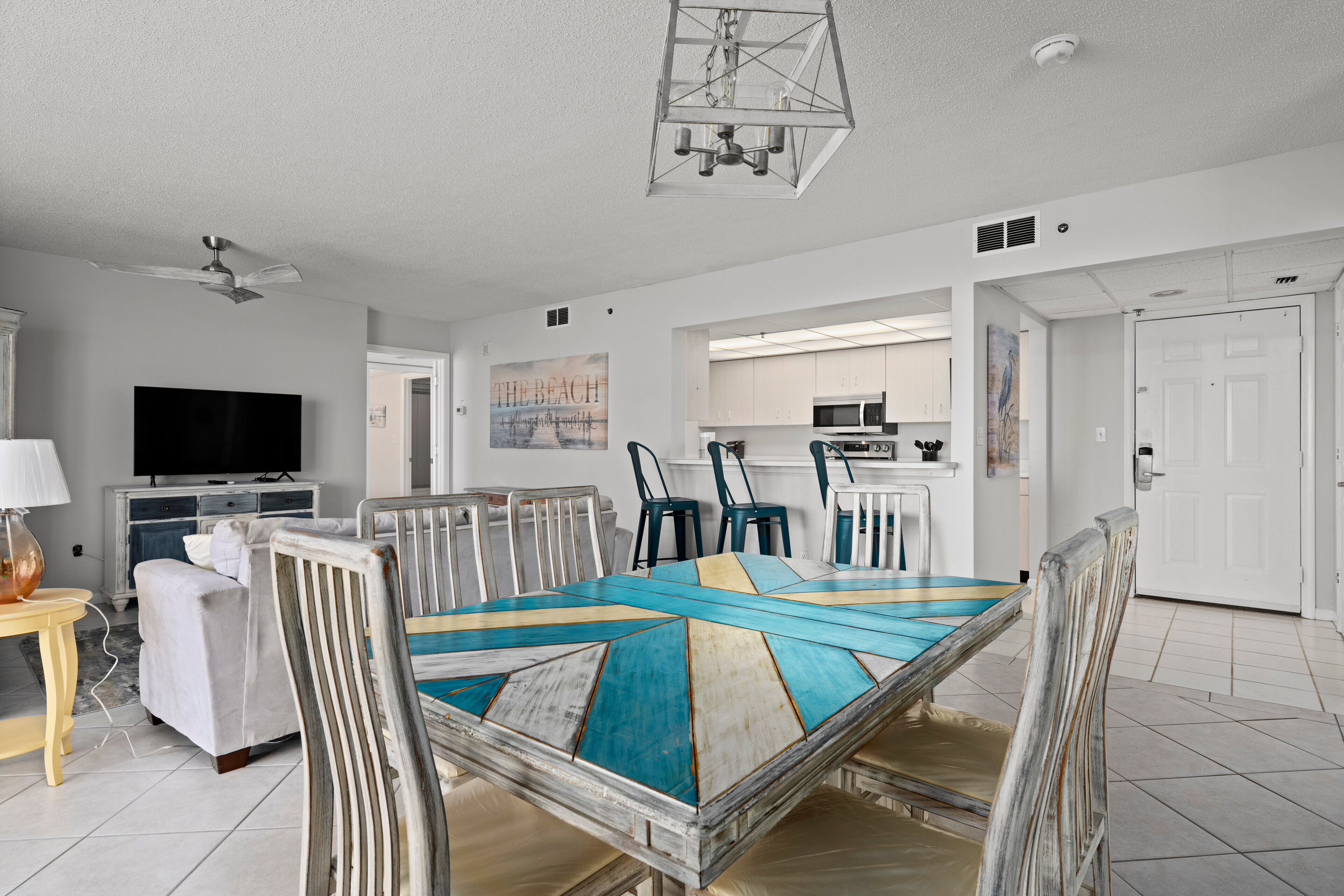 A spacious living room with a large dining table, a flat-screen TV, and a kitchen in the background.