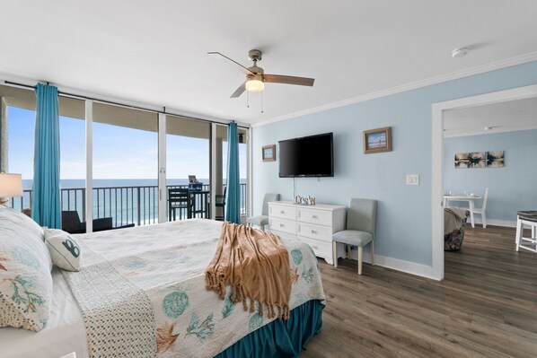 Un dormitorio con cama, televisor, cómoda, escritorio y balcón con vistas.