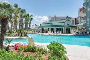 Un hotel con piscina, palmeras y una zona de estar cubierta.